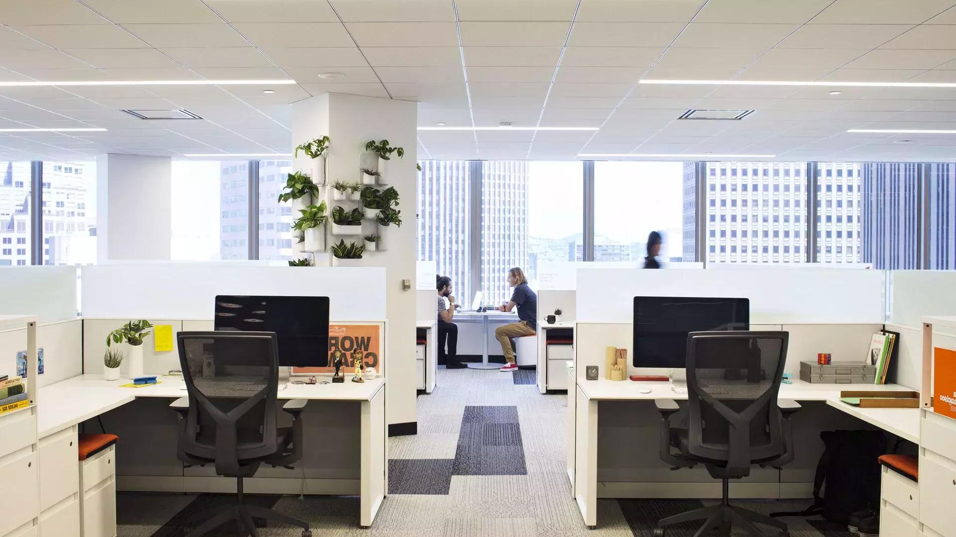 贝博体彩app办公大楼的内部场景。前景是一张桌子，两个人在大窗前的桌子上工作。。