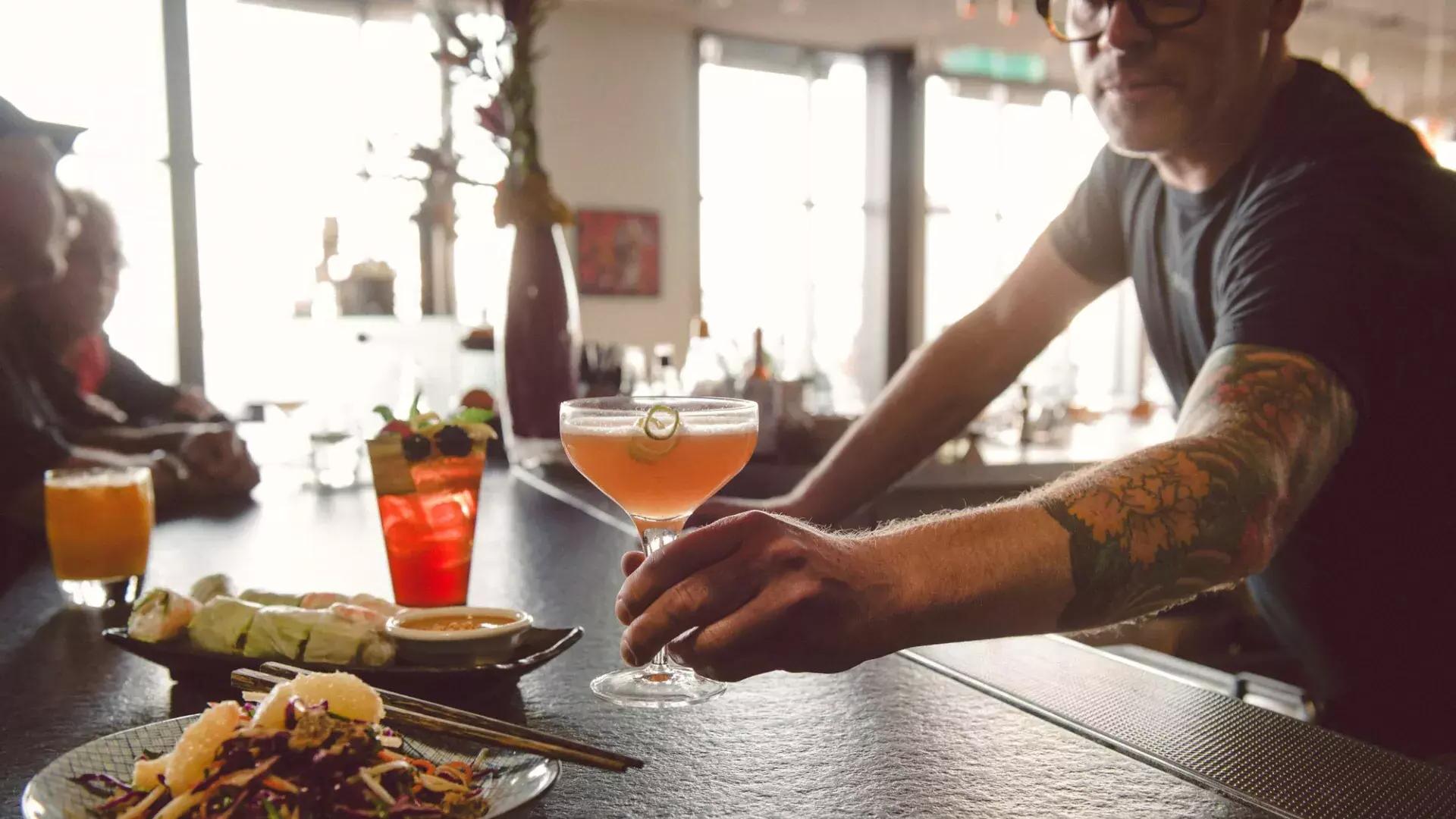 一个酒保在贝博体彩app的一家酒吧为顾客端来一杯鸡尾酒.
