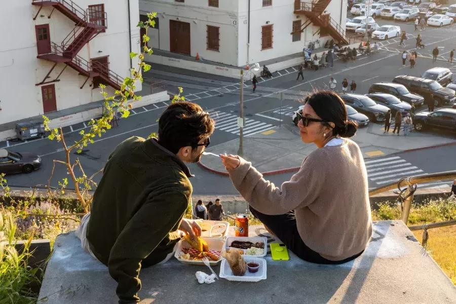サンフランシスコのフォート メイソン センターで屋外で食事をするカップル。女性は仲間に食べ物の味を与えます。