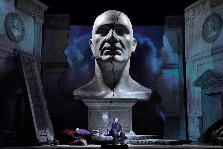 Um busto gigante de um homem paira sobre dois atores no palco de uma produção de Don Giovanni 在贝博体彩app.