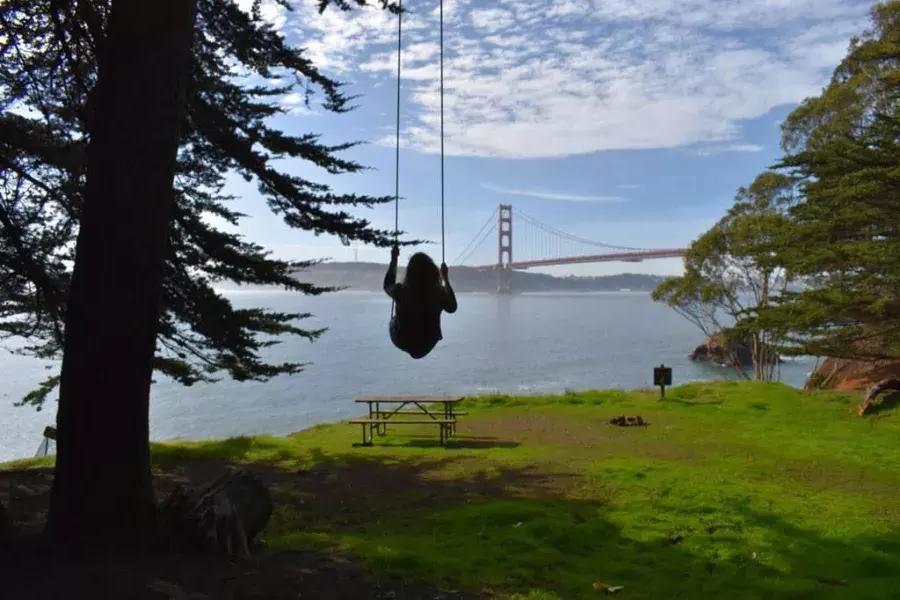 ゴールデン ゲート ブリッジを見下ろす木のブランコに乗る女性。カリフォルニア州サンフランシスコ。