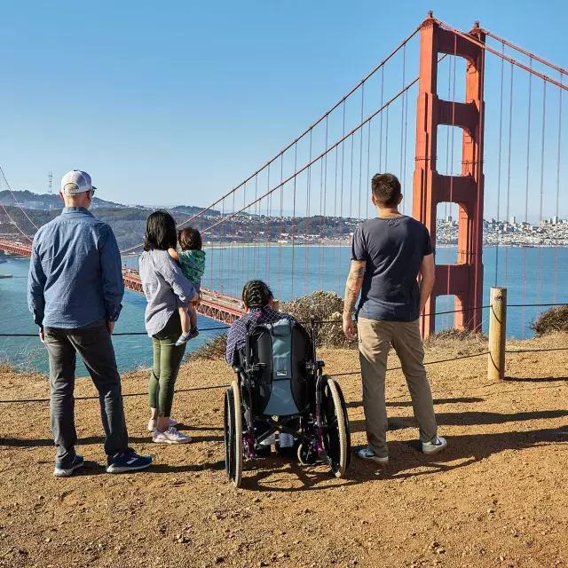 一群人, 包括一个坐轮椅的人, ist von hinten zu sehen, 从马林岬俯瞰金门大桥。.