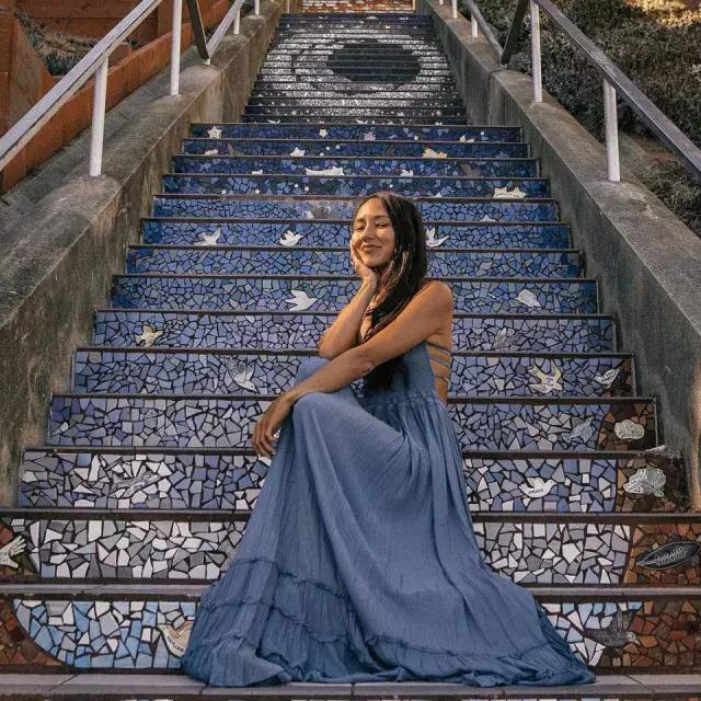 한 여성이 샌프란시스코 선셋 지역 16번가 타일 계단에 앉아 포즈를 취하고 있습니다.